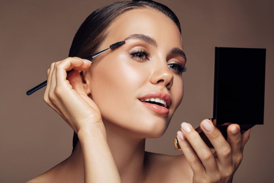 Woman applying minimalist makeup with eyebrow brush and compact mirror demonstrating natural beauty routine