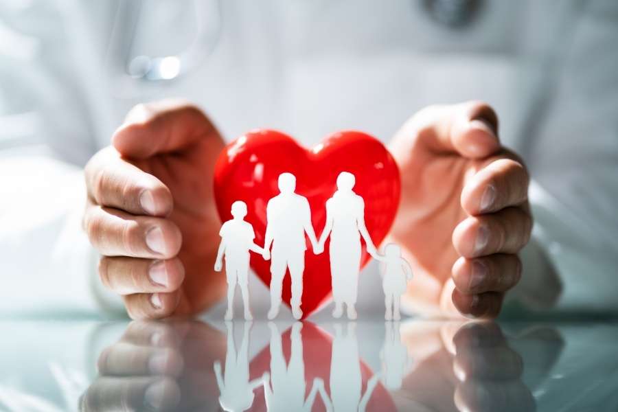 Protective hands surrounding family silhouettes and red heart symbolizing health insurance family coverage