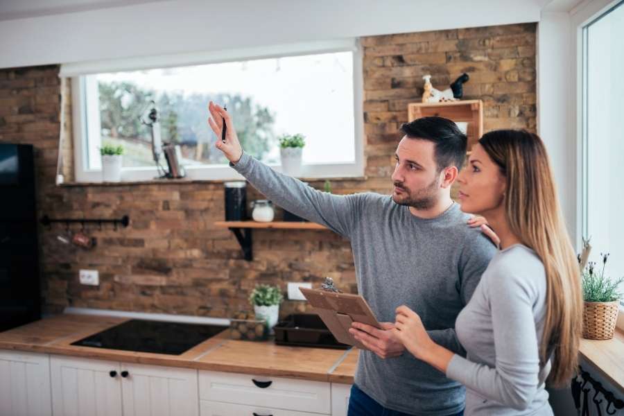 Young couple planning kitchen renovation with tablet and color samples in rustic kitchen with brick backsplash