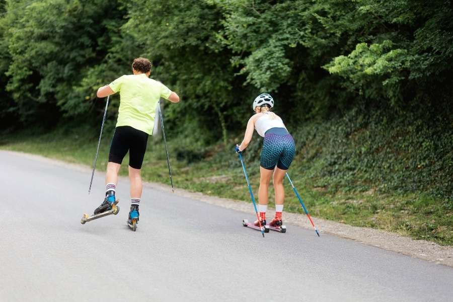 Two athletes roller skiing on path as part of Olympic training cross-country program