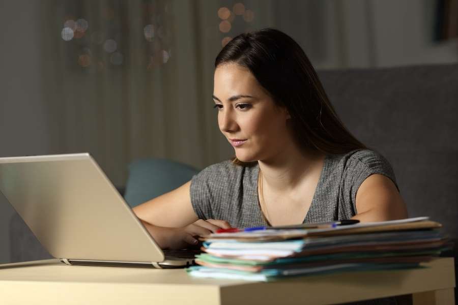 Dedicated student engaged in online learning through laptop with textbooks and study materials during focused evening session