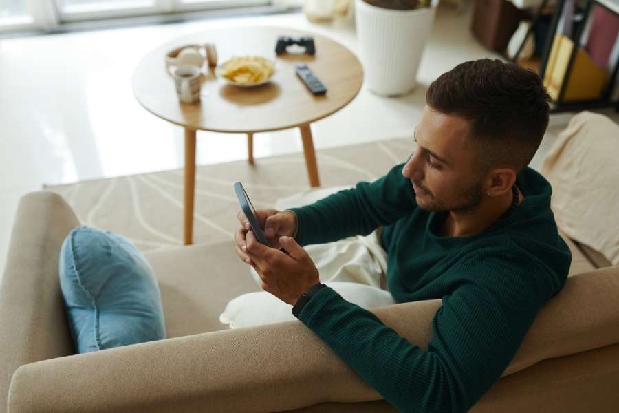 Young man relaxing on sofa while using smartphone showing social media's impact on daily leisure activities