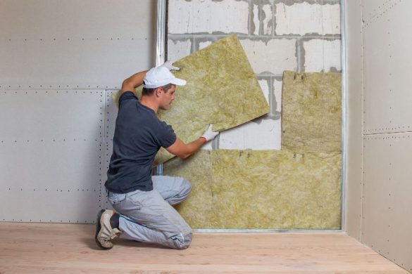 A worker installing mineral wool panels between wall studs, demonstrating how to go about insulating your home yourself.