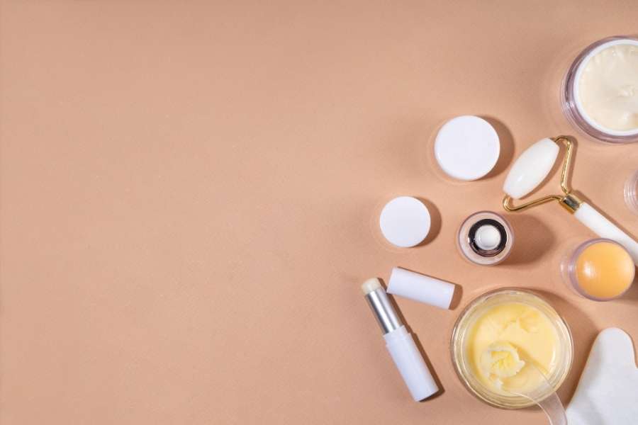 A flat lay of premium skincare tools and products including a jade roller, lip balm, and cream jars, representing the world of expensive skincare.