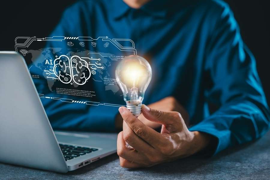 A man holding a glowing light bulb next to a laptop displaying a holographic artificial intelligence brain interface.