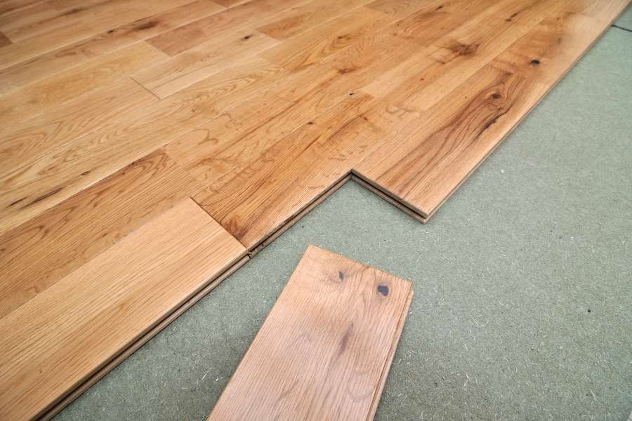 A close-up view of laminate wood flooring installation showing interlocking planks over an underlayment layer to fix creaky wooden floorboards.